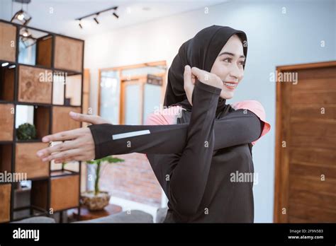 A Muslim Woman In Sports Clothes Stands Stretching With One Hand