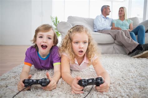 Siblings Playing Video Game While Parents Sitting On Sofa Stock Image