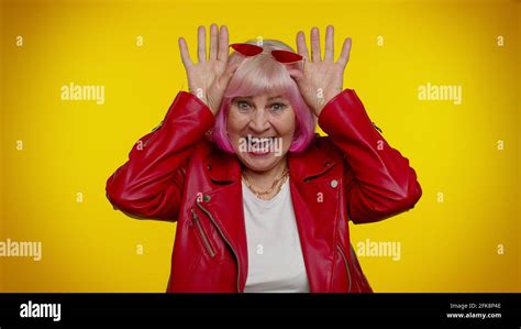 funny silly senior old granny woman smiling friendly and doing bunny ears gesture on head
