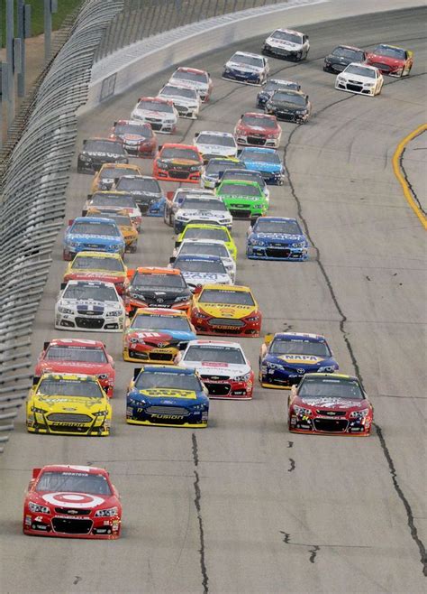A Large Group Of Cars Driving Down A Race Track With One Car In The Middle