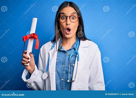 Young Beautiful Brunette Doctor Woman Wearing Glasses And Coat Holding Diploma Degree Scared In