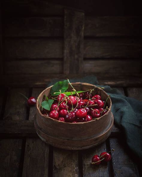 A Wooden Bowl Filled With Cherries On Top Of A Table