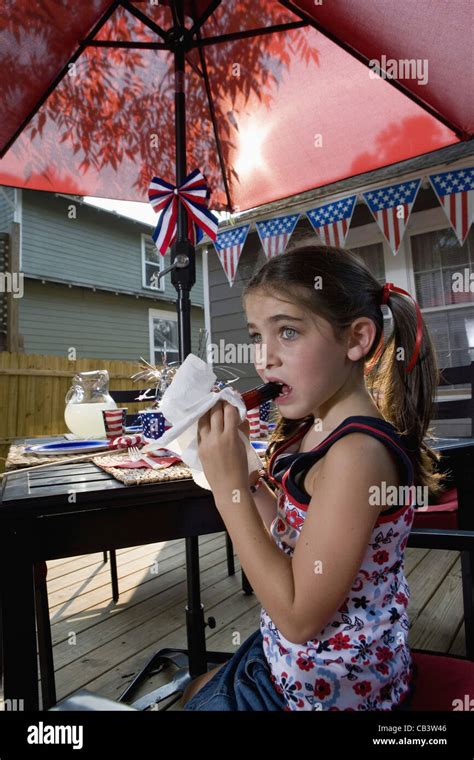 Girl Eating A Popsicle At Picnic Table In Backyard Patio With 4th Of July Decorations Stock