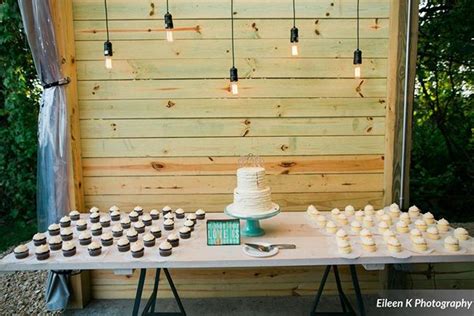 A Table With Cupcakes And A Cake On It In Front Of A Wooden Wall