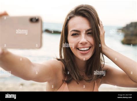 bild des lächelnden jungen frau in bh unter selfie foto auf handy während er auf sunny beach