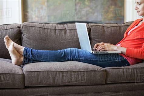 Mixed Race Caucasian Woman At Home On The Couch Working On A Lap Top Computer With Her Feet Up