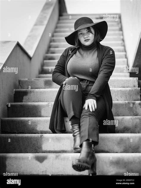 brunette woman in hat sitting on the stairs of building in city plus size model black and