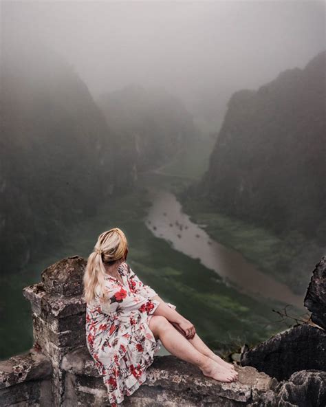 A Woman Sitting On Top Of A Rock Next To A River In The Foggy Mountains