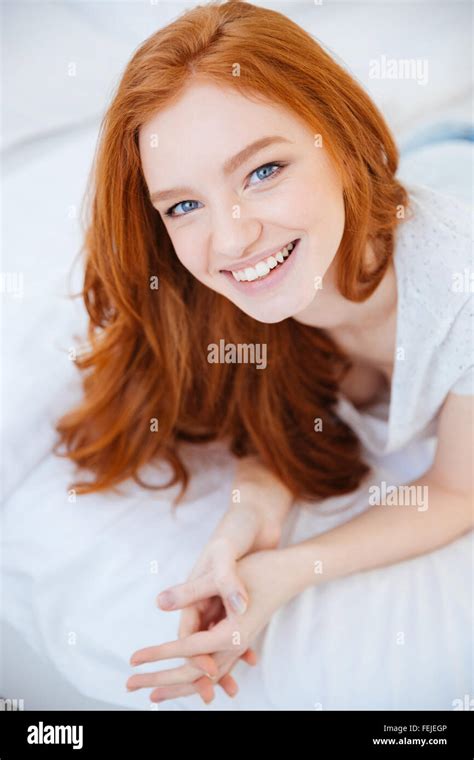 Smiling Redhead Woman Lying On The Bed At Home And Looking At Camera