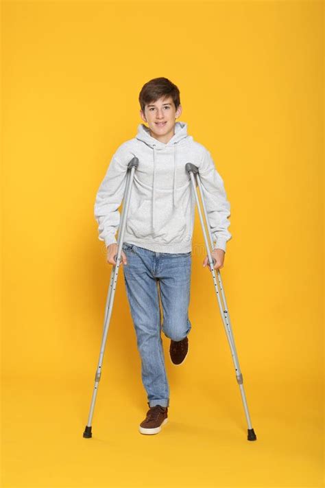 Teenage Boy With Injured Leg Using Crutches On Yellow Background Stock