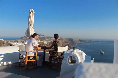 Two People Sitting At A Table On Top Of A Roof Overlooking The Ocean