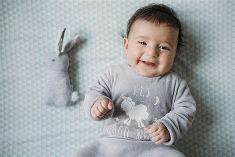 Portrait Of Smiling Baby Girl Lying On Bed Beside Toy Bunny Stock Photo