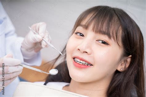 Asian Doctor Dentist Examine Female Patient With Braces In A Dental Office Wearing Gloves