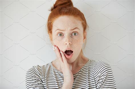 Young Redhead Woman With Surprised Facial Expression Looking At The Camera Screaming With Mouth