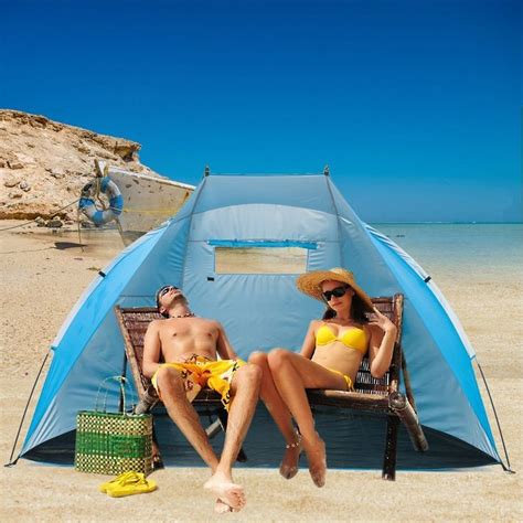 Two People Sitting In Chairs On The Beach Next To A Blue Tent And A Boat