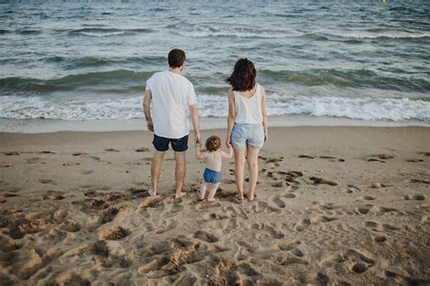 Husband And Wife With Son Looking At View While Standing On Beach