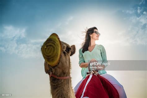 Low Angle View Of Female Tourist Riding Camel In Desert Dubai United