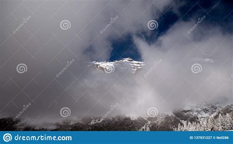A Snow Capped Mountain Top Pokes Through The Clouds And Mist In The