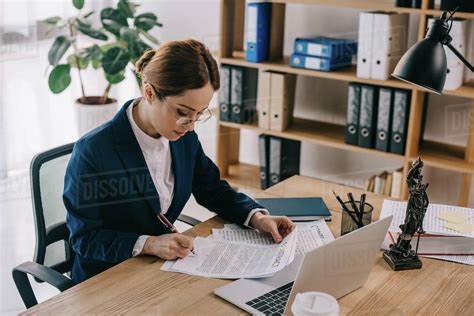 Side View Of Female Lawyer Doing Paperwork At Workplace With Laptop In