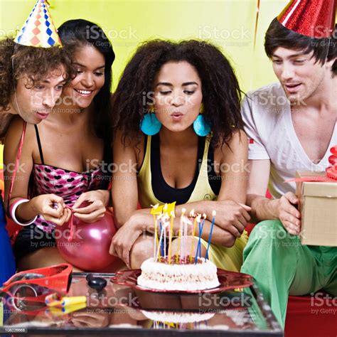 Young Woman Blowing Candles On Birthday Cake Celebrating With Friends