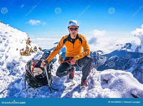 Climber On A Mountain Top Posing On The Background Of Snowy Mountains