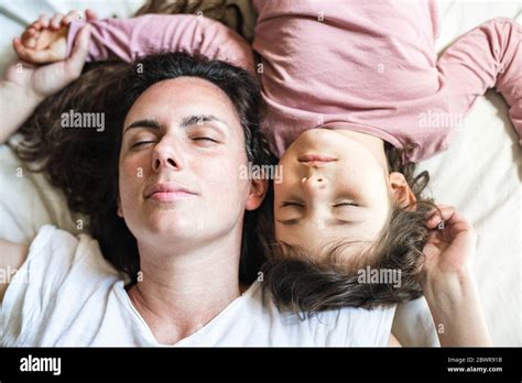 Mother And Daughter Lie Down In Bed With Their Heads Facing Up Their Eyes Are Closed Having A