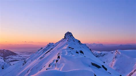 A Mountain Covered In Snow At Sunset With The Sun Setting On Its Horizon