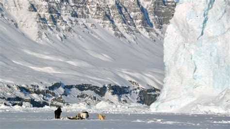 Some People Are Standing In The Snow Near An Iceberg With Mountains In