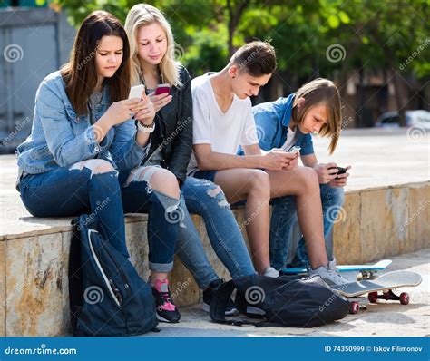 Portrait Of Four Teenagers Sitting With Their Mobile Phones Outdoors