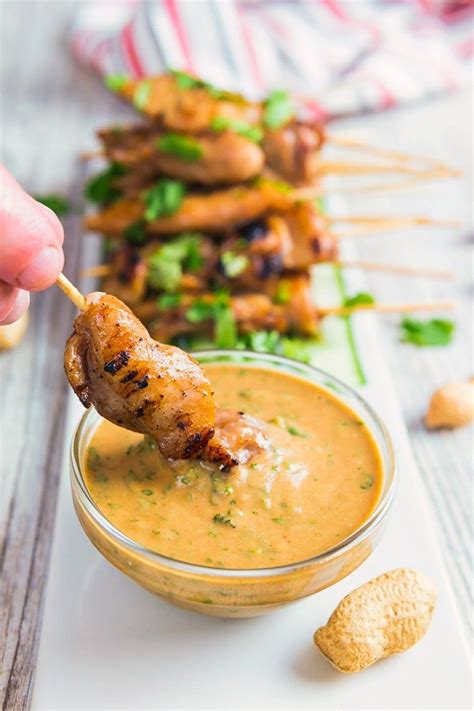 Chicken Satay Being Dipped In A Glass Bowl Of Peanut Dipping Sauce
