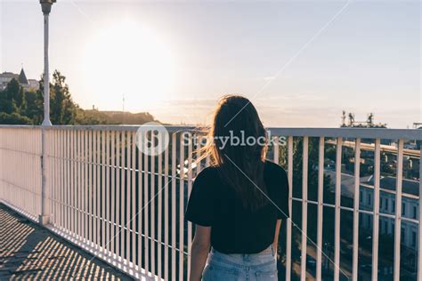 A Slender Brunette Girl Is Walking Along The Bridge In Summer During Sunset View From The Back