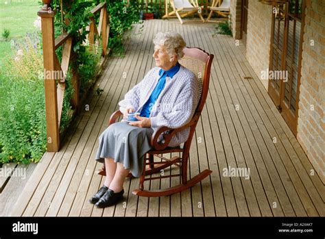 Old Woman Sitting In Rocking Chair On Veranda At Home Stock Photo
