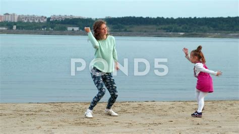 Happy Mother And Daughter Dancing And Jumping In Front Of Wild Ocean In
