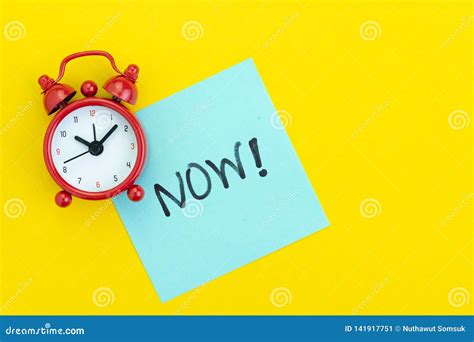 Sticky Post With Handwriting The Word Now With Red Alarm Clock On Solid