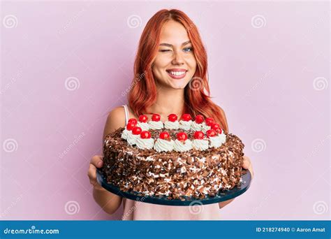Young Redhead Woman Celebrating Birthday With Cake Winking Looking At The Camera With Expression