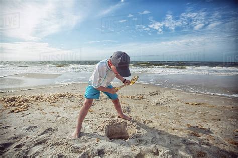 Boy On Beach Digging Hole In Sand Stock Photo Dissolve