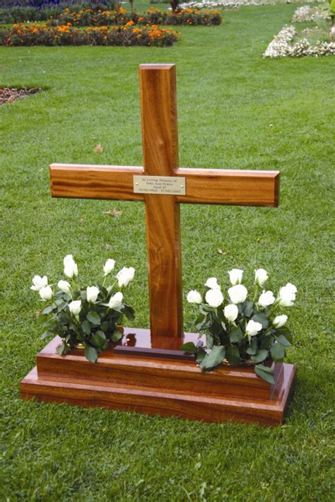 A Wooden Cross Sitting On Top Of A Lush Green Field Next To Flowers And