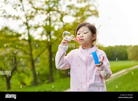 Asian Girl Is Blowing Fragile Soap Bubbles In The Park In The Summer