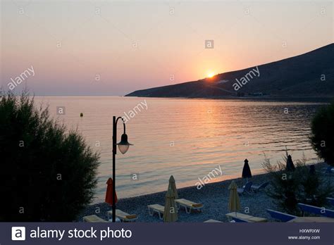 sunrise over the bay of livadia with pebbled beach sunshades and street lamp in foreground