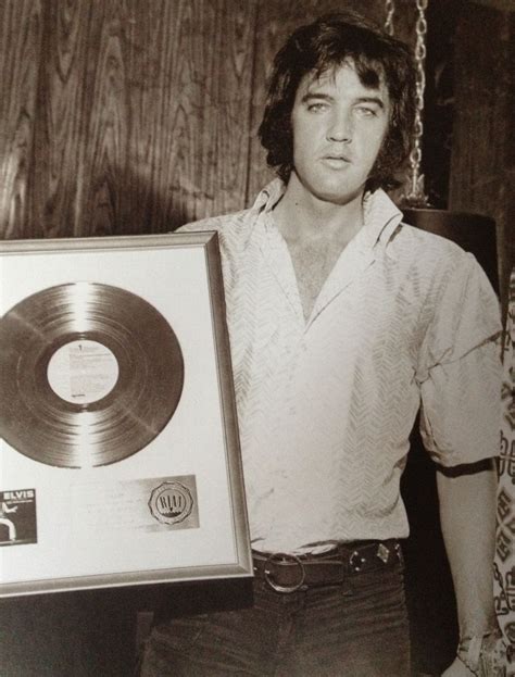 A Man Holding Up A Record In Front Of A Wooden Wall With Chains Hanging