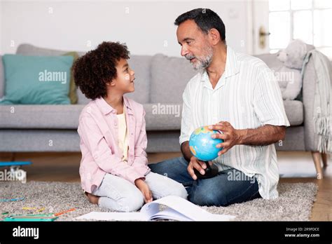 Latin Grandpa Talking To Grandson Holding World Globe At Home Stock