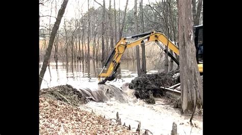 breaking beaver dam on 10 acre pond flooded excavator trackhoe caterpillar digging out mud
