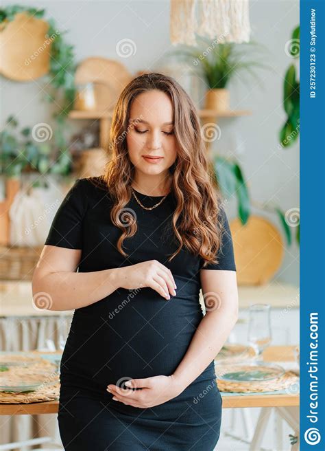 beautiful pregnant woman in black dress touches the stomach in the home interior stock image