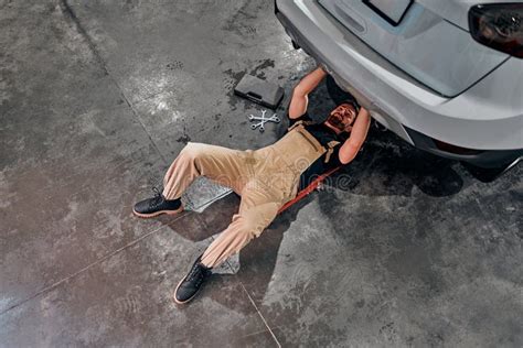 Mechanics In Uniform Lying Down And Working Under Car At The Garage