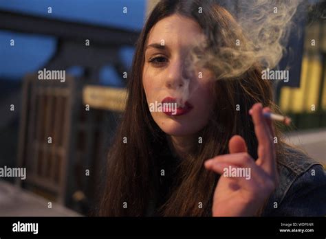 Close Up Of Young Woman Smoking Cigarette In City At Night Stock Photo
