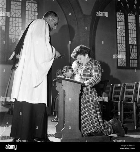 Woman Kneeling At The Altar Praying In Church Watched By Her Priest