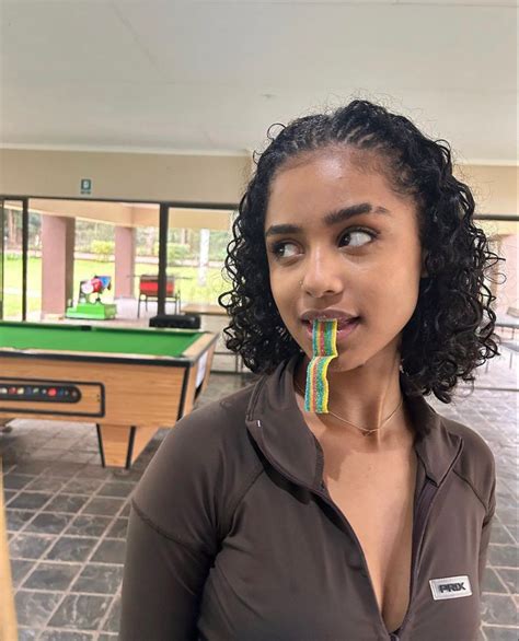 a woman with curly hair is holding a candy bar in her mouth
