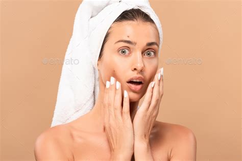 surprised naked girl touching face with pimples and looking at camera isolated on beige stock
