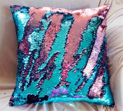 A Pink And Blue Sequin Pillow Sitting On Top Of A White Couch Next To A