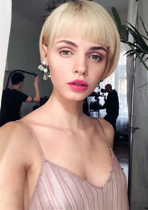 a woman with short blonde hair and pink lipstick wearing a dress in front of a mirror